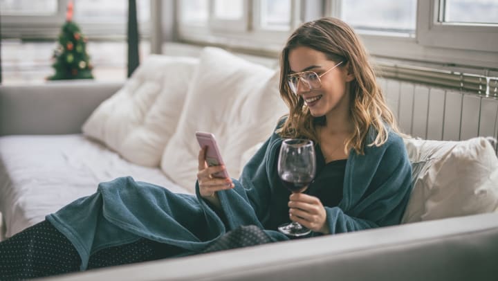 A woman scrolling through her phone while enjoying a glass of wine from wine delivery services in Sedona.