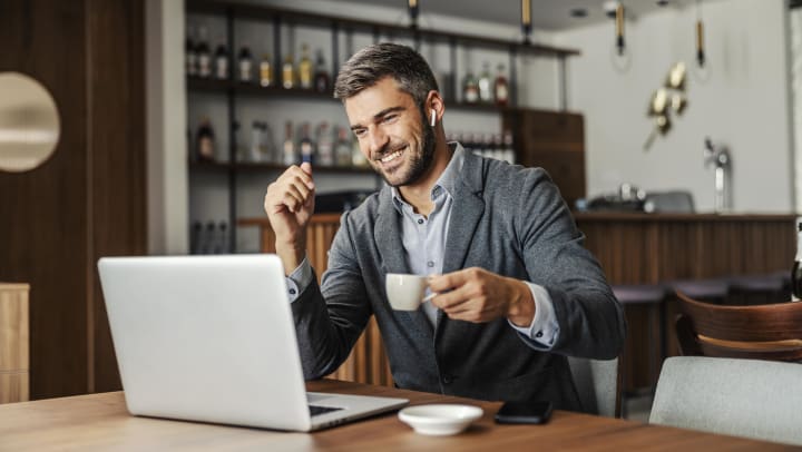 A man smiling while looking at his laptop while he sit at a table in a Gilbert coffee shop.