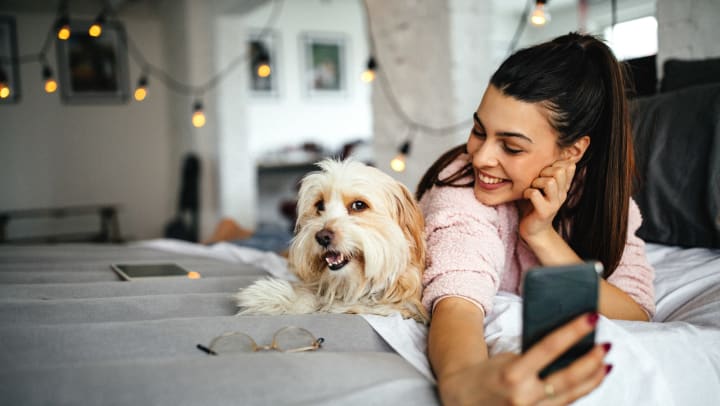 Smiling dog owner taking a selfie with her dog on her bed at Anatole on Briarwood