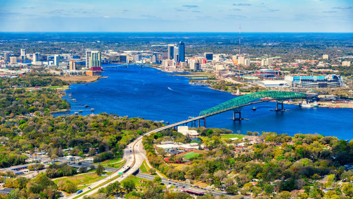 Aerial view of downtown Jacksonville with river, bridge, high-rise buildings, and trees on a sunny day