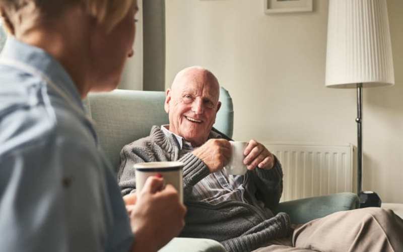 Resident enjoying a cup of coffee with a caregiver at The Pineapple House at Sapphire Lakes in Naples, Florida