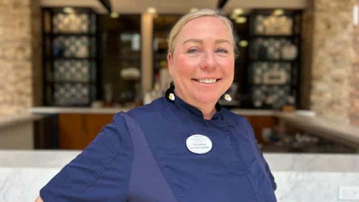 Chef Amy Lebrun smiling in her navy chef coat, standing confidently in front of the modern open kitchen at Clearwater Living in Newport Beach