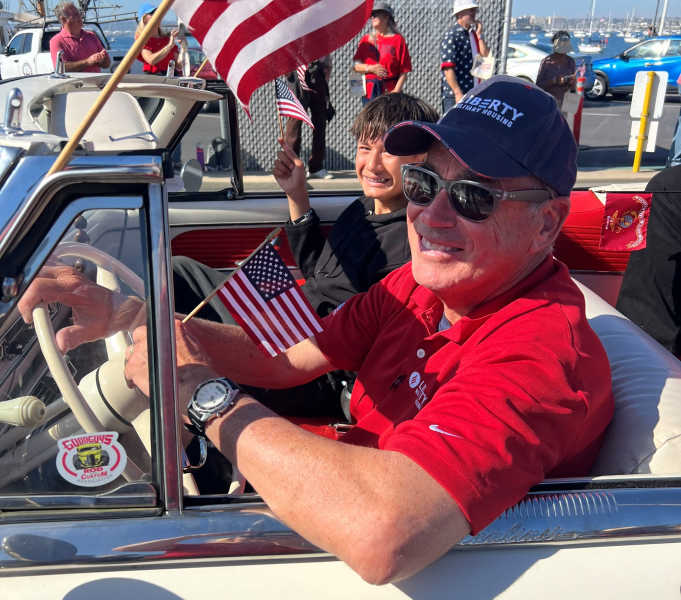 Man in convertible car along side a young boy driving through the San Deigo Fleet Week Veterans Parade