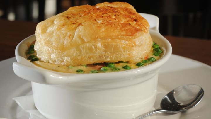 A white ceramic bowl of chicken pot pie with a biscuit on top.