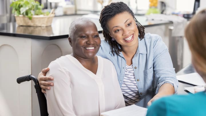 Senior woman in a wheelchair and younger woman smiling and looking toward person in foreground.