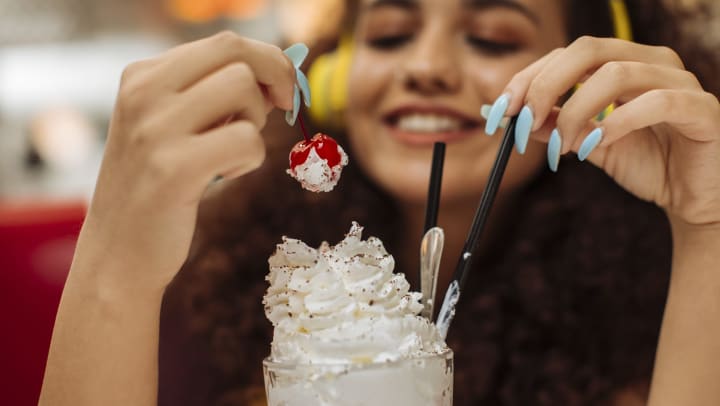 A smiling woman with headphones on holding up the cherry from her milkshake.