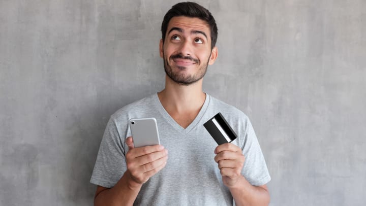 Man with contemplative expression holding credit card and phone