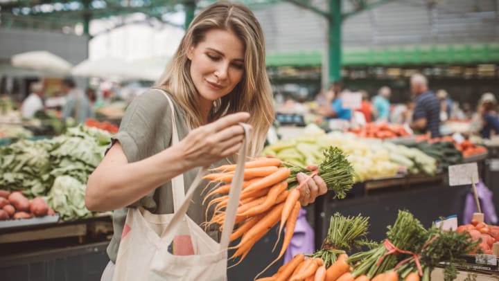 A woman at a farmers market putting carrots in a bag. 