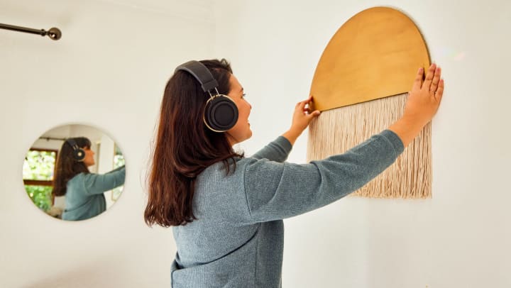 Young woman wearing headphones and hanging an art piece on the wall. 