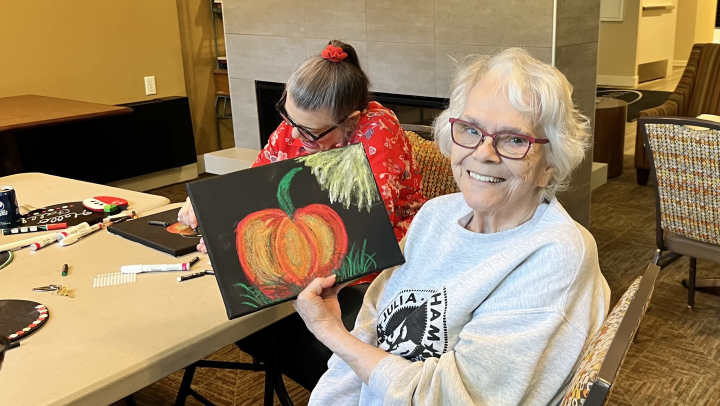 Woman holding up a painting of a pumpkin during craft time