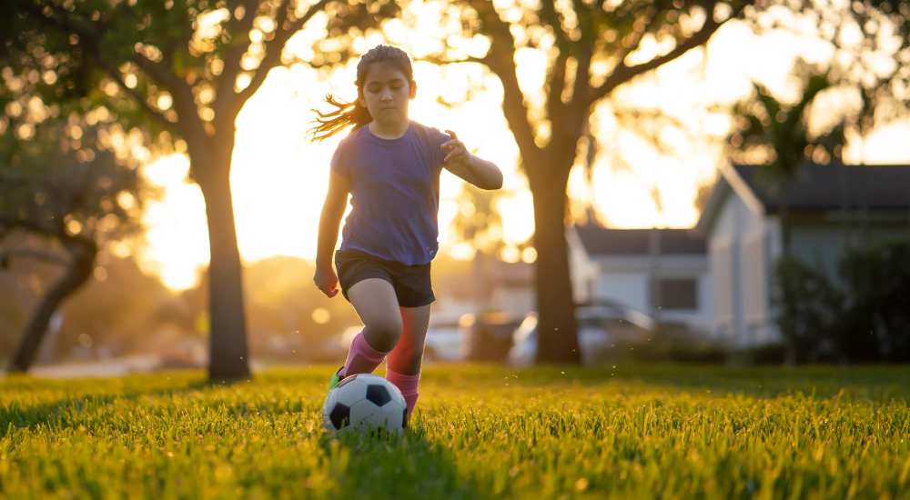 Child playing soccer with a ball on a sunlit grassy lawn at Country Oaks in Weatherford, Texas