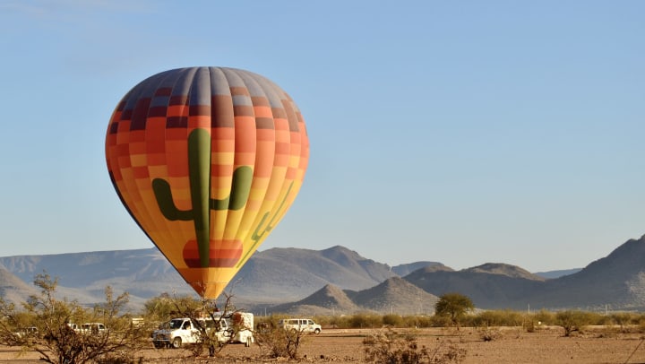 A hot air balloon with giant cactuses painted on it in the middle of a desert.