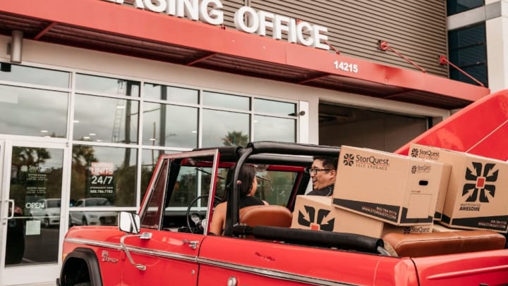 Couple in vehicle filled with moving boxes parked in front of a StorQuest leasing office