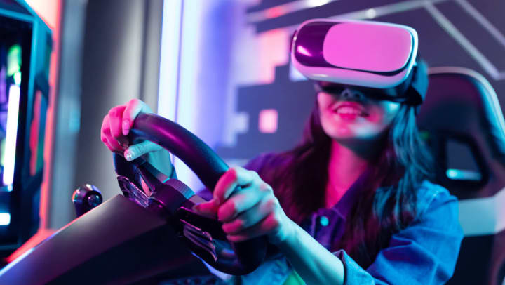 A smiling woman wears a VR headset while gripping a steering wheel as she plays a game at a virtual reality arcade in Savannah