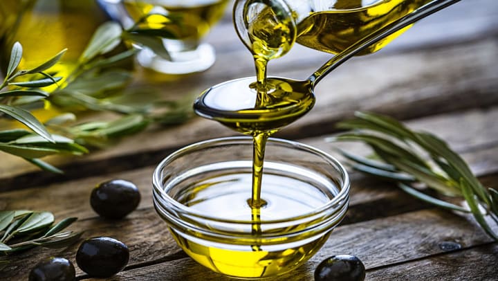 Pouring extra virgin olive oil from a spoon to a glass container.