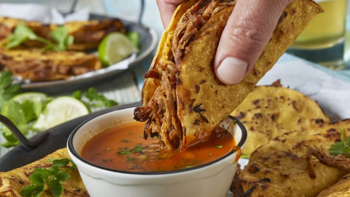 dipping a taco in birria sauce