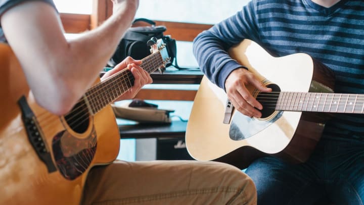 Student learning how to play the guitar with a teacher