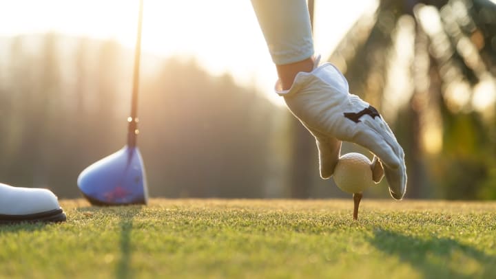 A close-up of a golfer placing a ball on a tee.