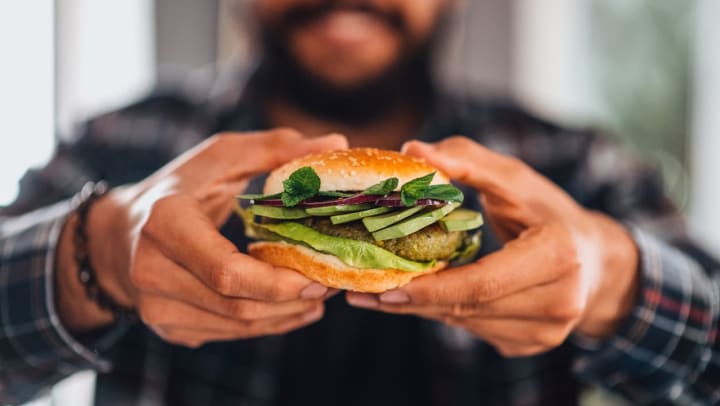 Man Holding a vegan burger towards the camera