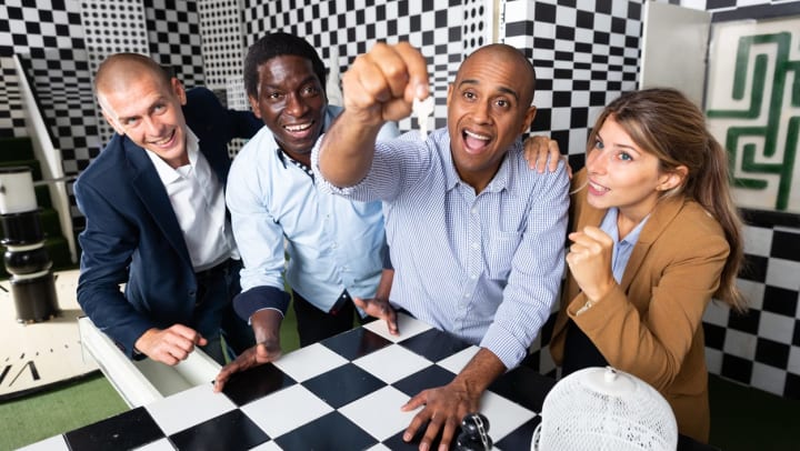 Four people in a checker patterned room with one person holding up a key