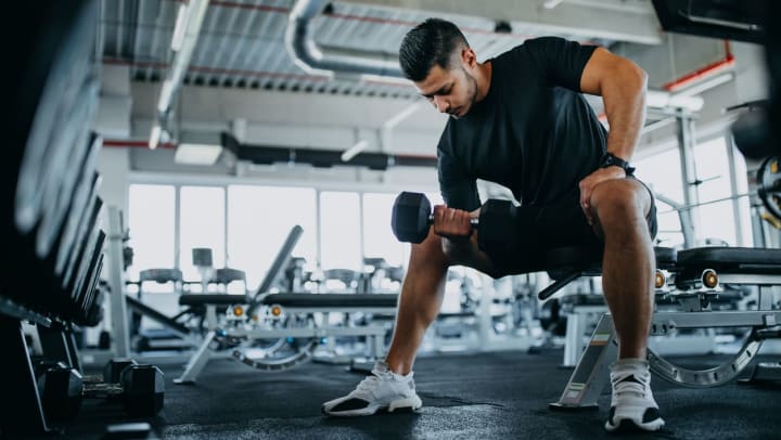 man sitting on a gym bench while doing bicep curls | fitness centers in Santa Fe