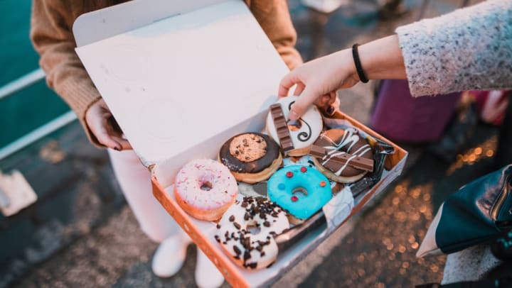 A hand reaches into a varied box of beautiful donuts