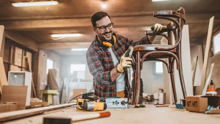 A man smiling while sanding a chair