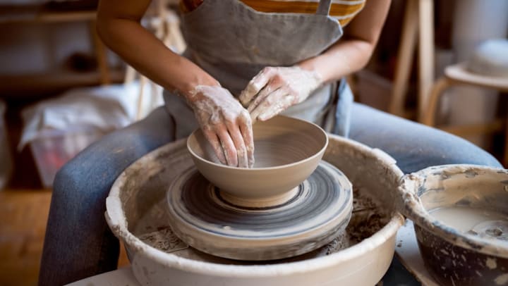 A female potter wearing an orange and white striped shirt creating a bowl on a pottery wheel | art studio in Casper