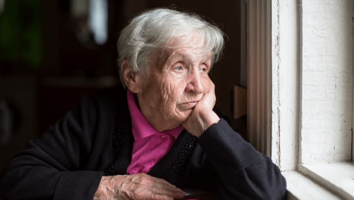 Elderly woman looking sadly out a window 