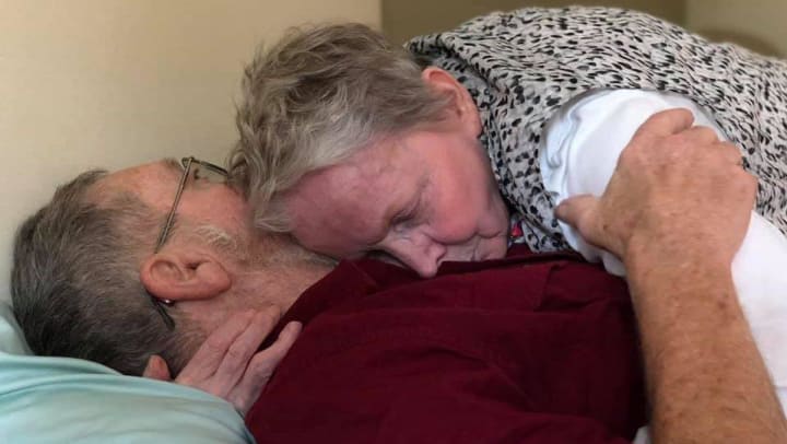 Resident hugging her husband who is laying in bed