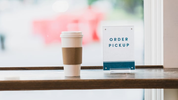 Takeout cup of coffee next to order pickup sign