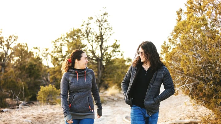 A smiling young man and woman walk side-by-side along a desert trail. 
