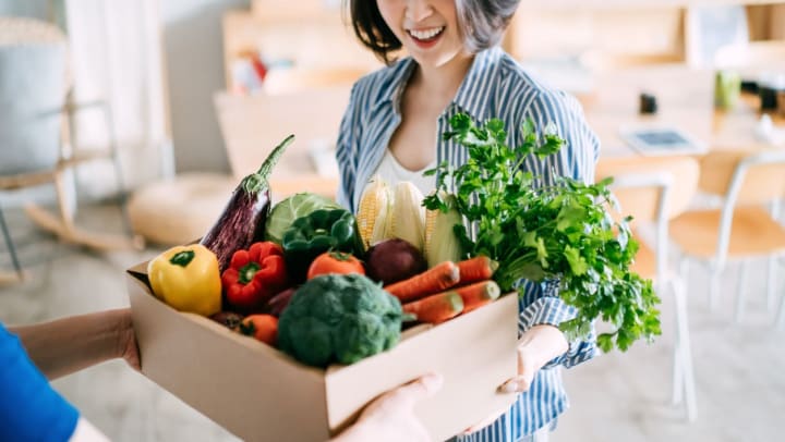 A woman getting handed a box of vegetables