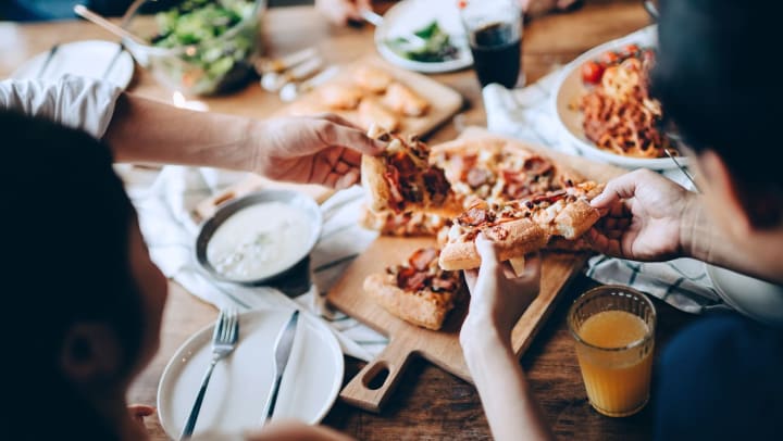 An overhead view of 3 people grabbing slices of pizza on a table | pizza near Casper