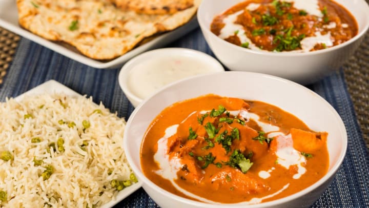Bowls of butter chicken curry, lamb vindaloo, basmati rice, and naan bread at an Indian cuisine restaurant in Albuquerque.