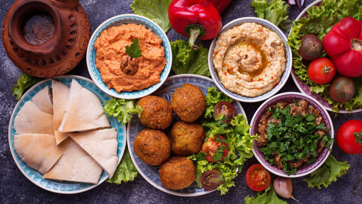 A selection of plant based foods served in colorful bowls sit on a dark table top garnished with kale greenery, tomatoes, onions, and peppers