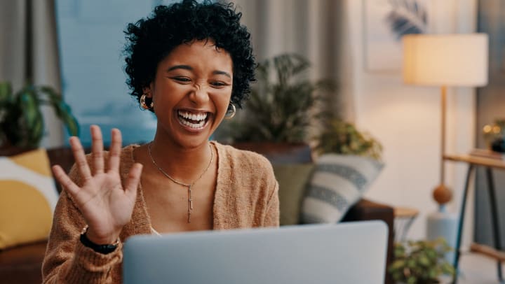 Woman smiling with her hand up in front of an open laptop. 