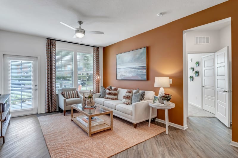 Model living room with plank flooring and large windows at Tapestry Westland Village in Jacksonville, Florida