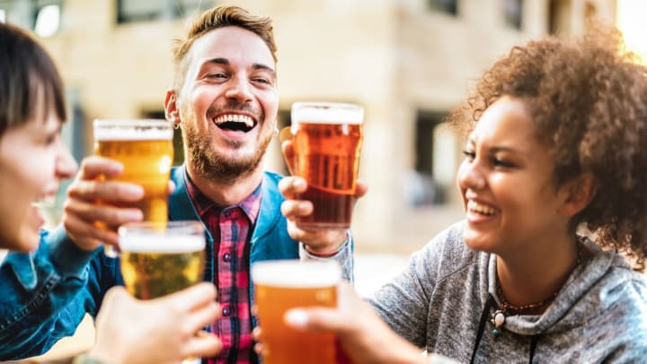 A group of laughing friends toast with full glasses of beer outdoors