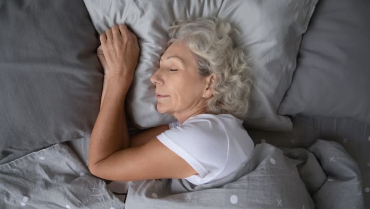 Older woman lying in bed with her eyes closed.