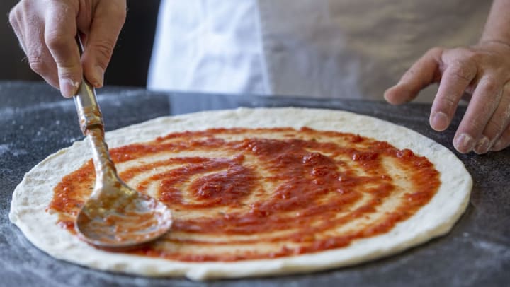 a pizza chef spreads red sauce on dough at a local pizzeria in Savannah