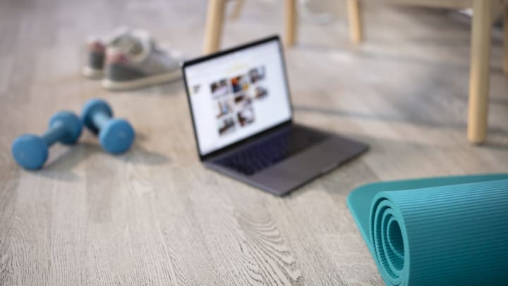 Mat, dumbbell, shoes, and laptop set out on a floor