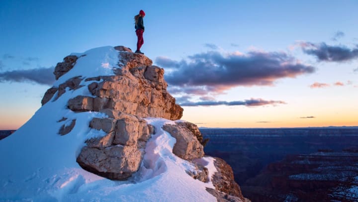 Woman stands on snowy peak at sunset 
