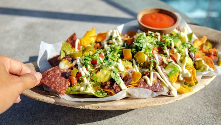 Person eating a plate of loaded nachos with cheese, ground beef, guacamole, and cilantro