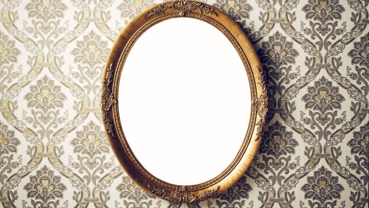Vintage, gold mirror hanging on a wall with wallpaper
