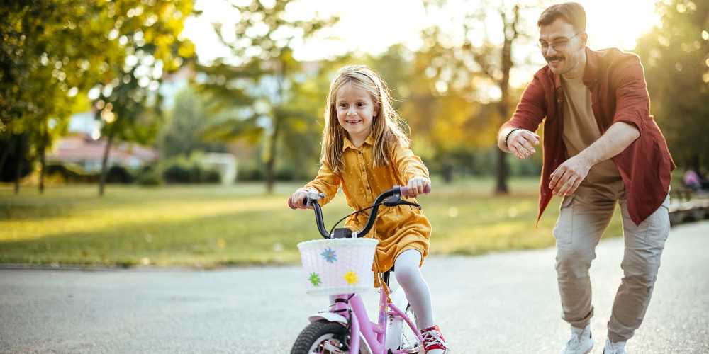 Father encouraging daughter on pink bicycle near The Mason in Augusta, Georgia