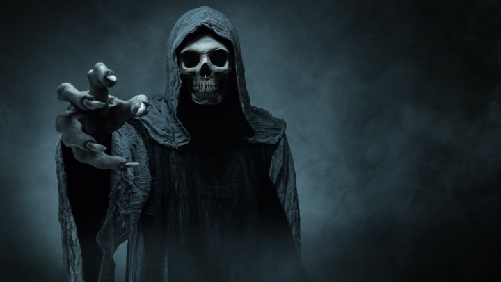 Scary hooded skeleton reaching out with a claw in a dark fog 