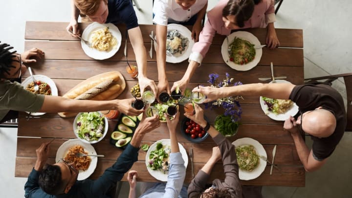 a group of friends gathered around a wood table doing a cheers at a dinner party | tips for hosting a dinner party