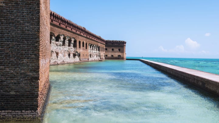 The historic brick fortress Fort Jefferson on Garden Key in Dry Tortugas National Park in Florida. A wall surrounds the former military outpost. Tropical-colored saltwater fills the moat and surrounding wall.