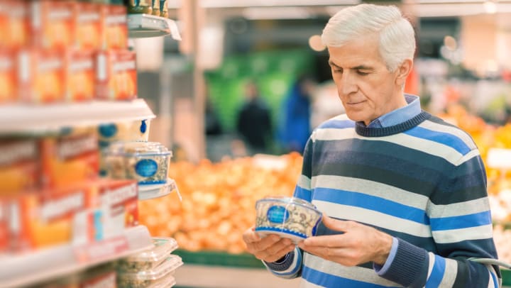 Elderly man shopping in local supermarket. He is holding box and reading nutrition label